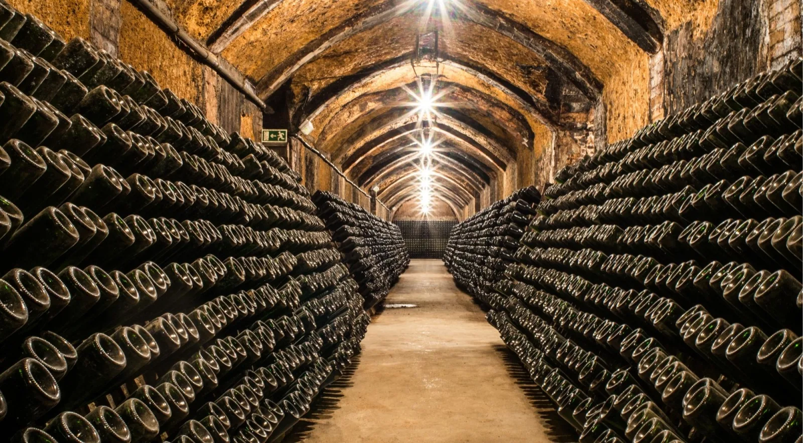 A long chalk cellar tunnel lined floor to ceiling with stacked, dust-covered Champagne bottles