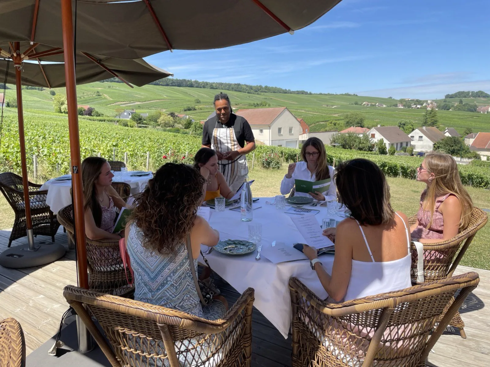 Guests seated under a parasol for lunch at a table overlooking the vineyards