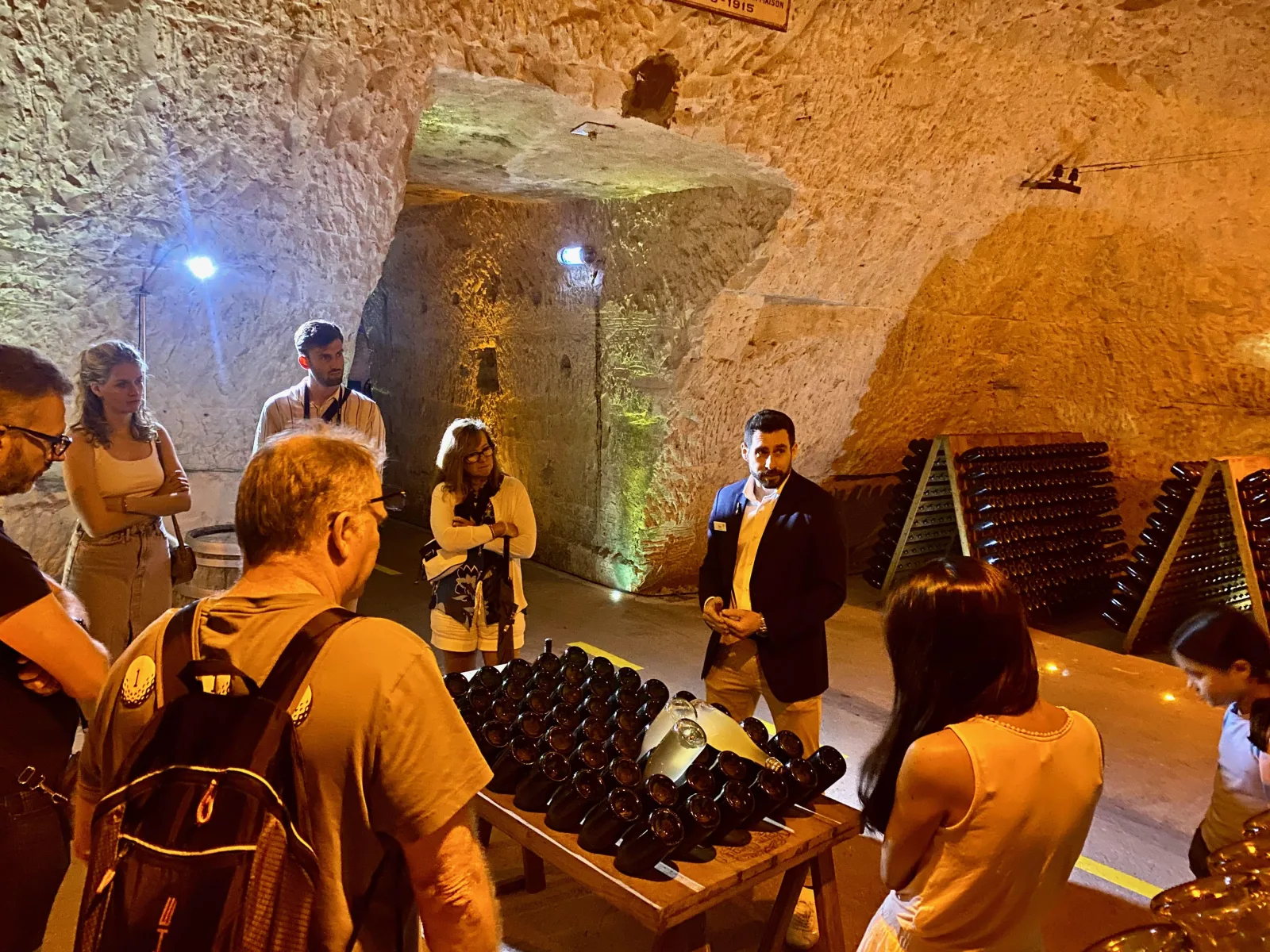 A guide showing bottles on a riddling rack to a small group in a chalk crayère