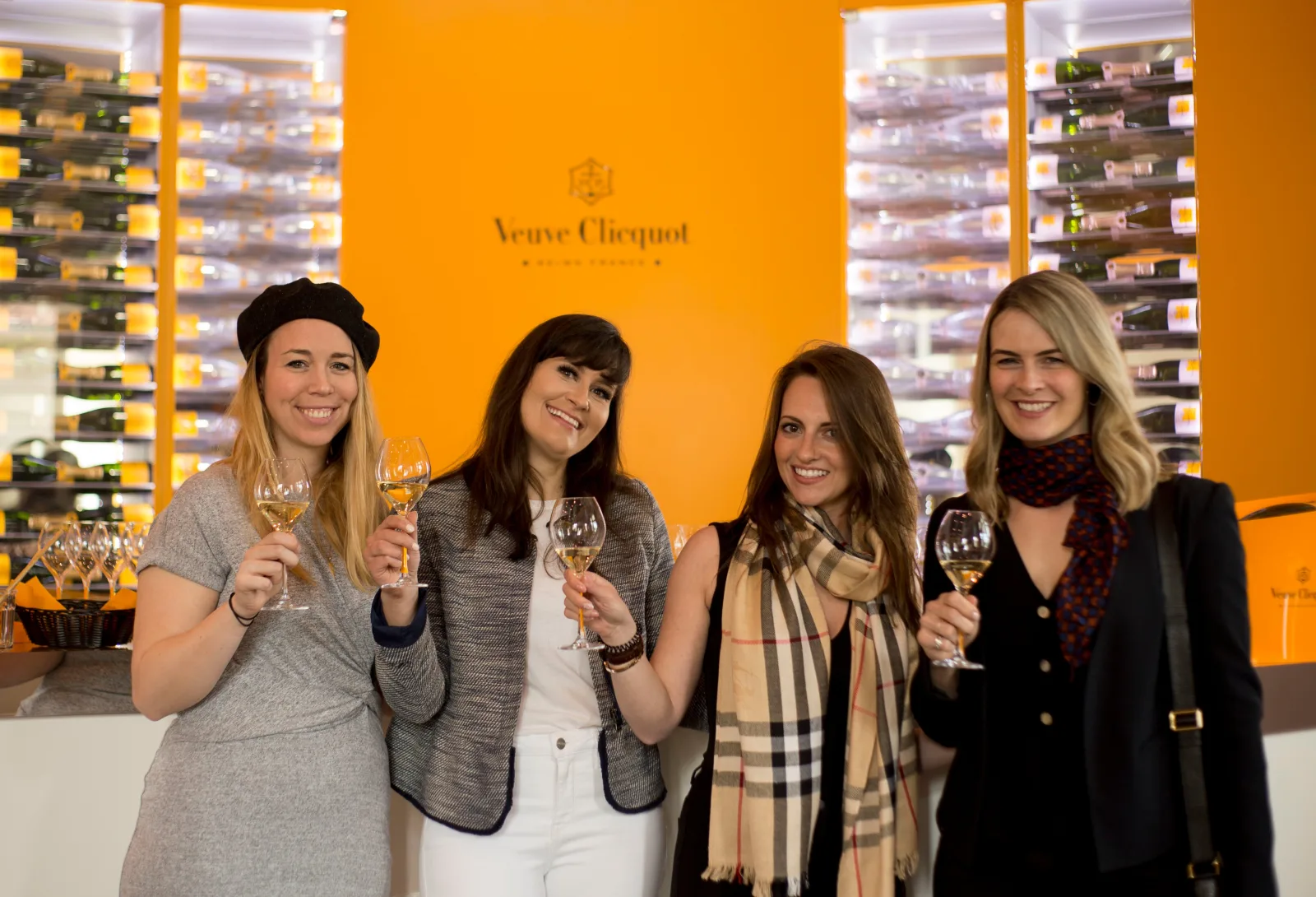 Four guests with flutes in front of the orange Veuve Clicquot tasting-room wall