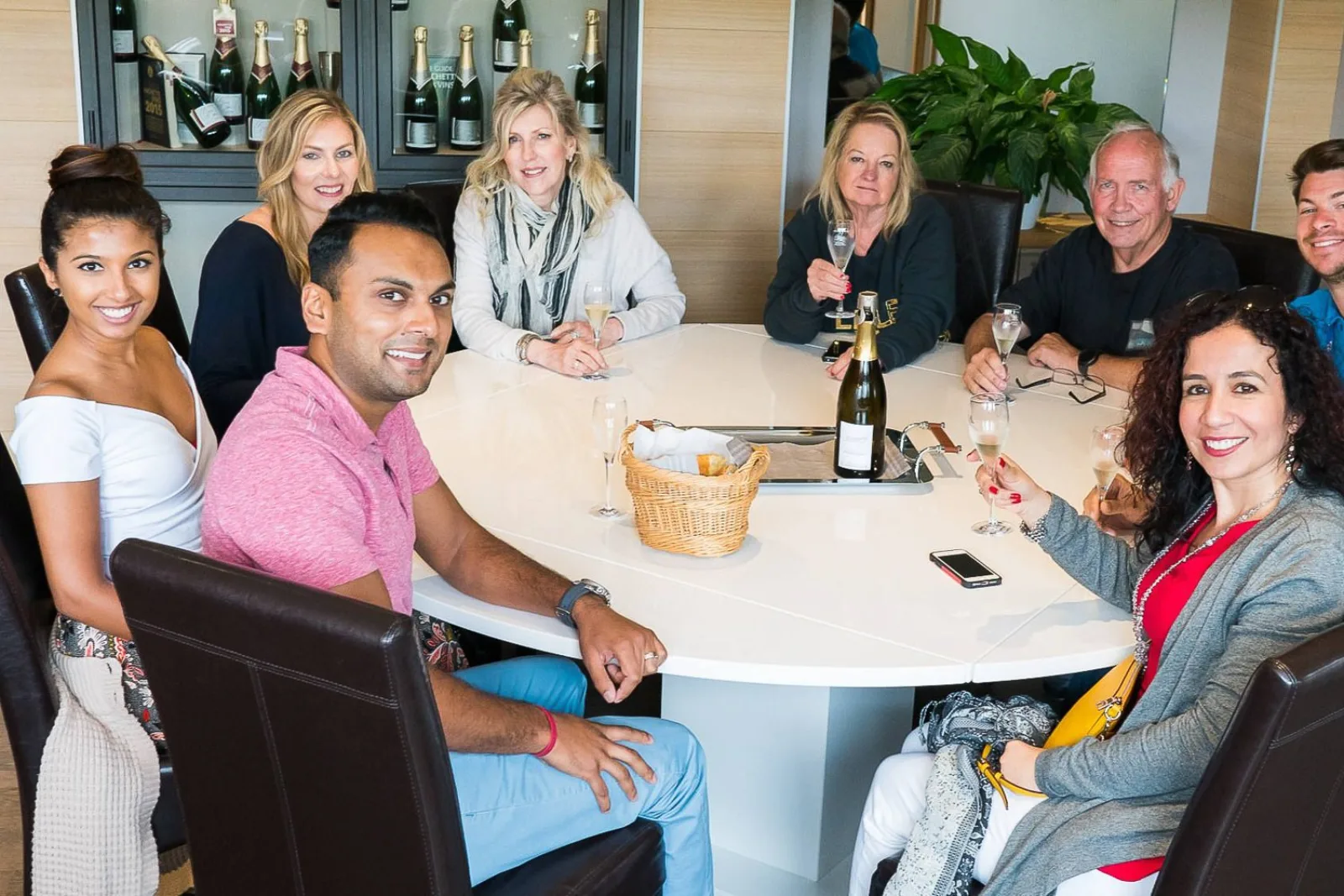 The small group seated around a table for a Champagne tasting, bottles displayed behind