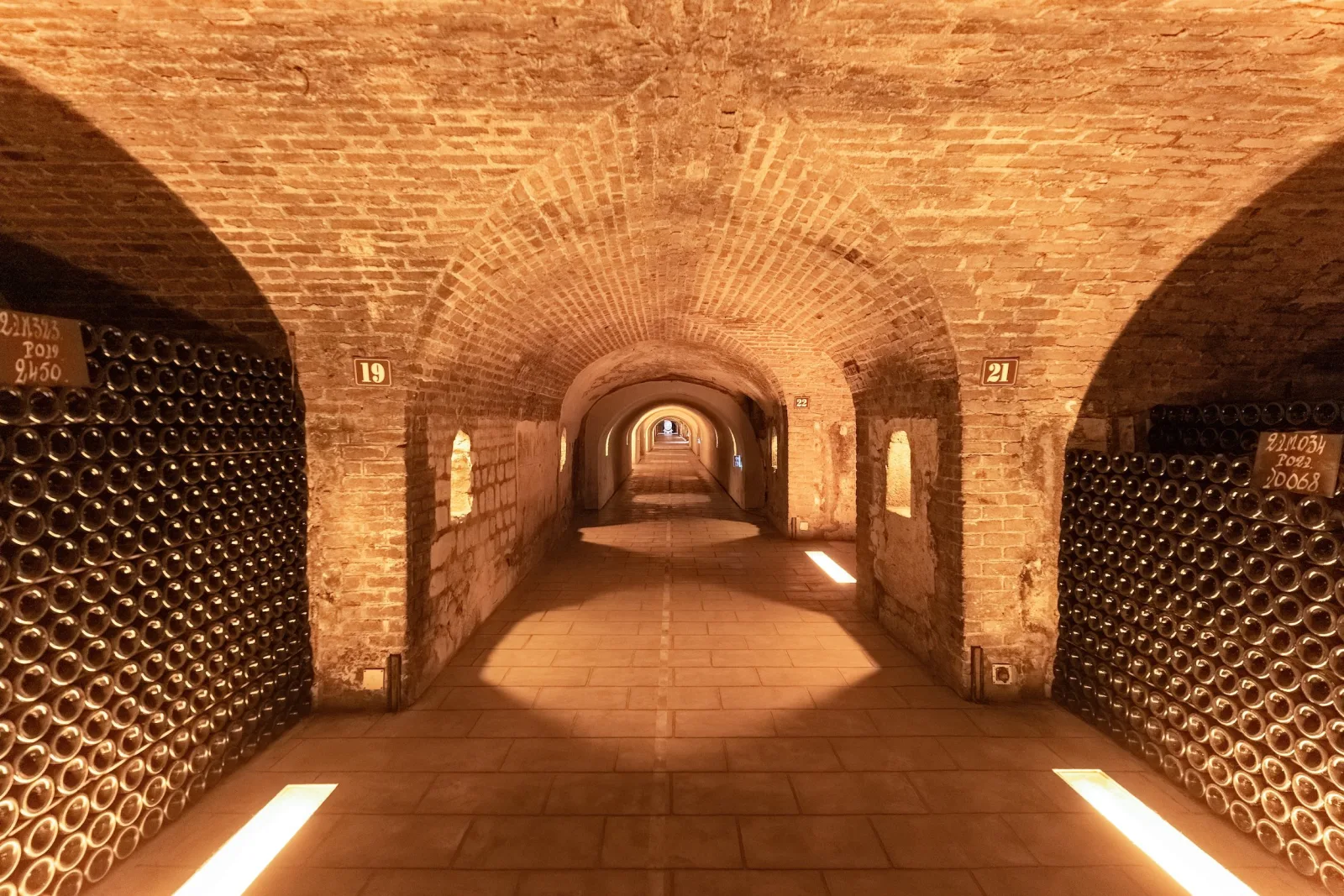 A vaulted brick cellar gallery stacked floor to ceiling with ageing Champagne bottles